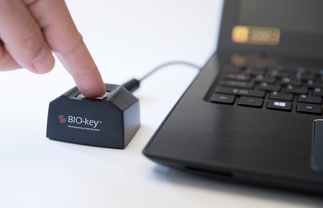 Someone using a fingerprint scanner plugged into a modern laptop on a white surface.